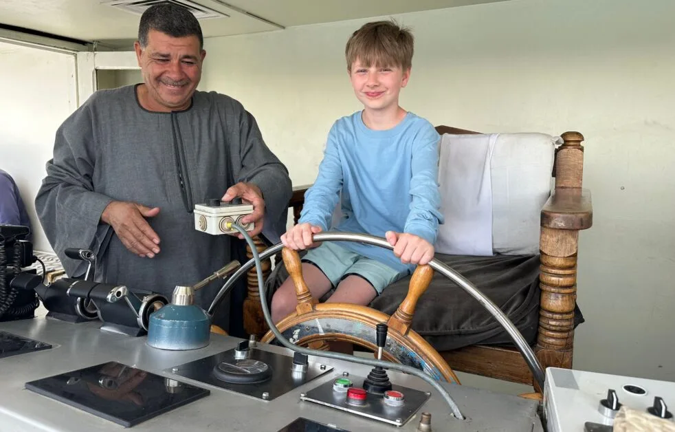 Child at the wheel of a Nile River boat with captain watching on.