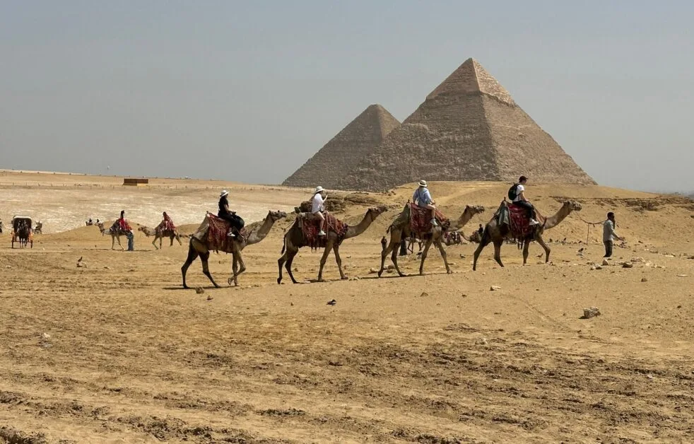 Tourists on camels exploring the Great Pyramids of Giza.