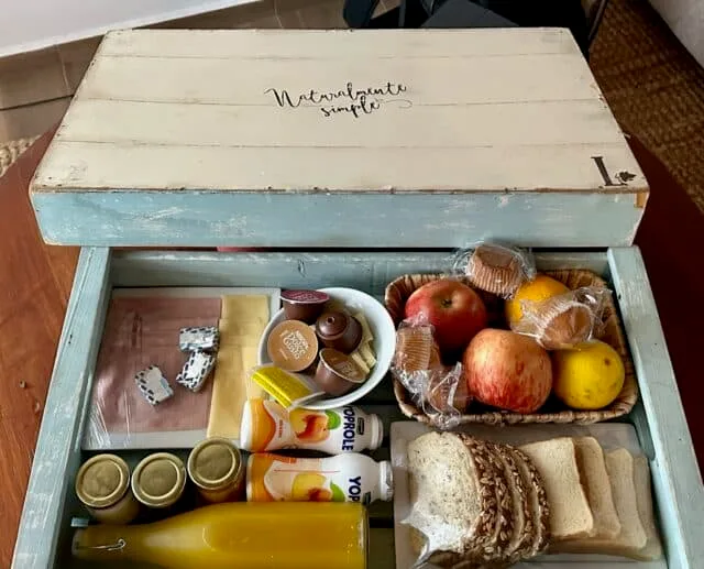 A box of breakfast foods including coffee, fruit, muffins, ham, cheese, and bread.