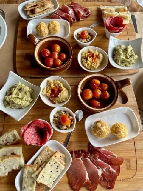 Hams, salami, crackers, cheese balls, hummus, and tomatoes were served as part of a wine-tasting event.