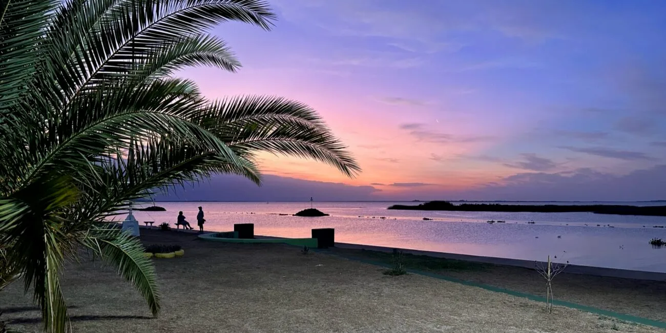 Sunset over the water with blue, purple, orange, and yellow colours in the sky.
