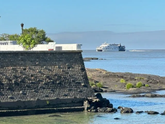 3-day itinerary in Southwest Uruguay. Harbour wall with trees in the background. A ferry is coming towards the port of Colonia having crossed a river.