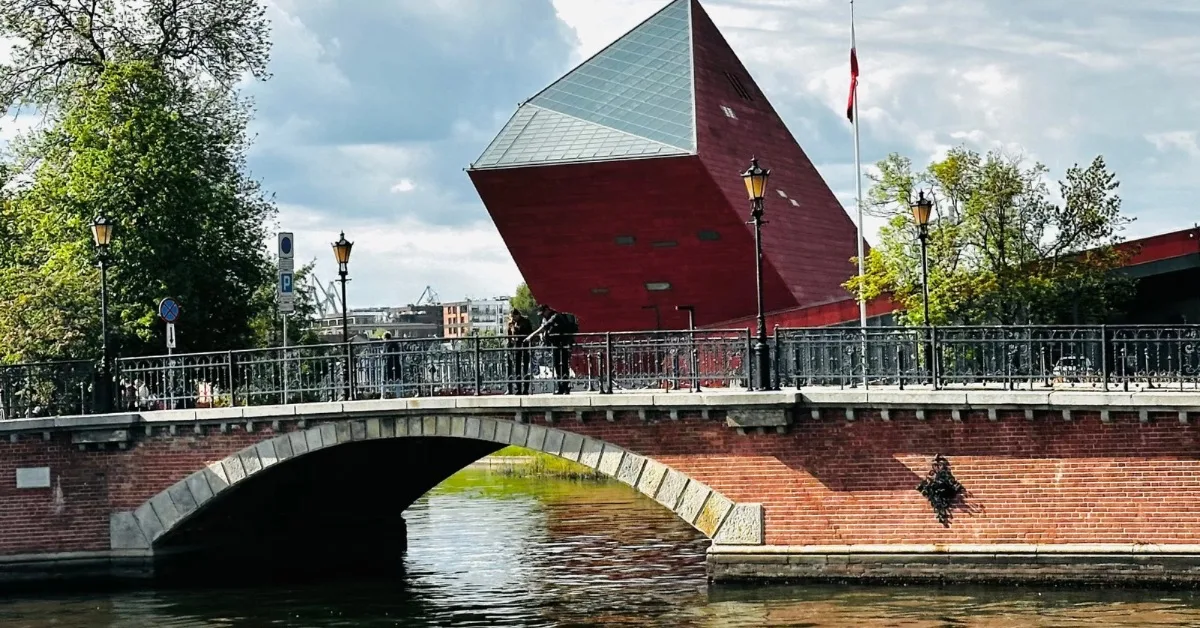 A modern glass angled building with red brick base and a bridge in Gdansk.