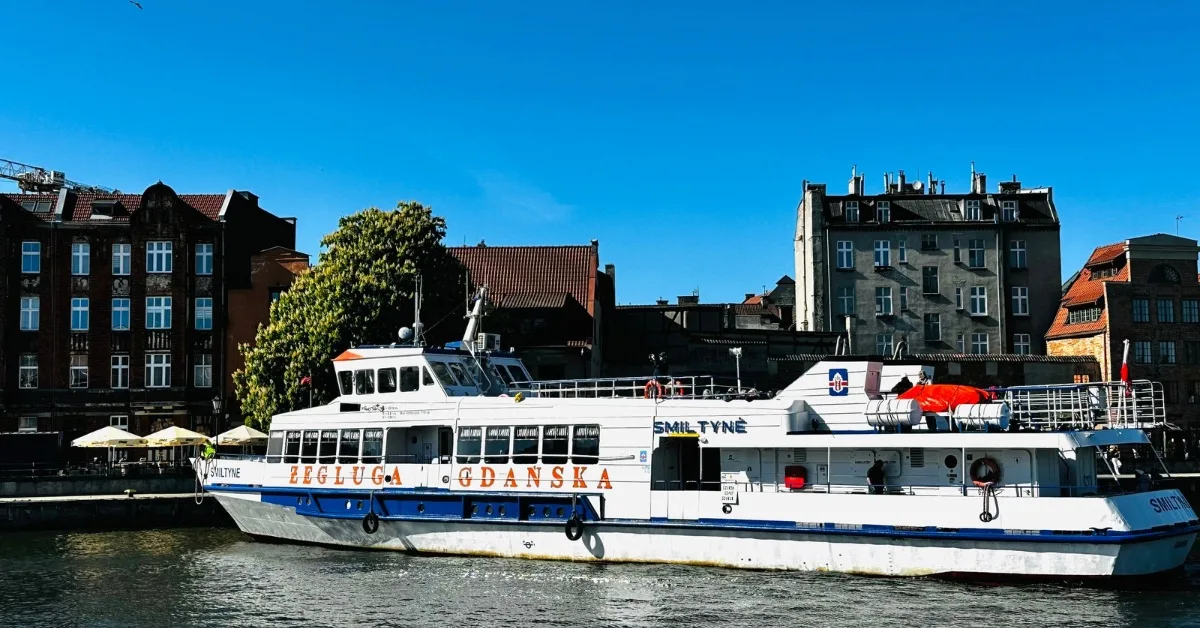 A white tour boat maneuvering on a river in Gdansk.