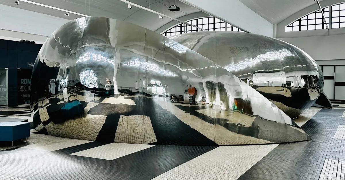 A room with a Large stainless steel modern art shaped in bow of ships against a black and white floor.