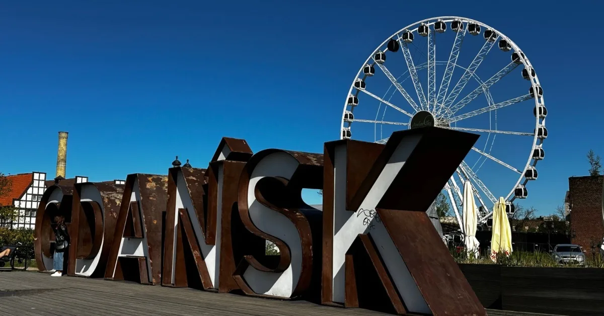 Over sized Gdansk sign in front of a large white Ferris wheel ride.