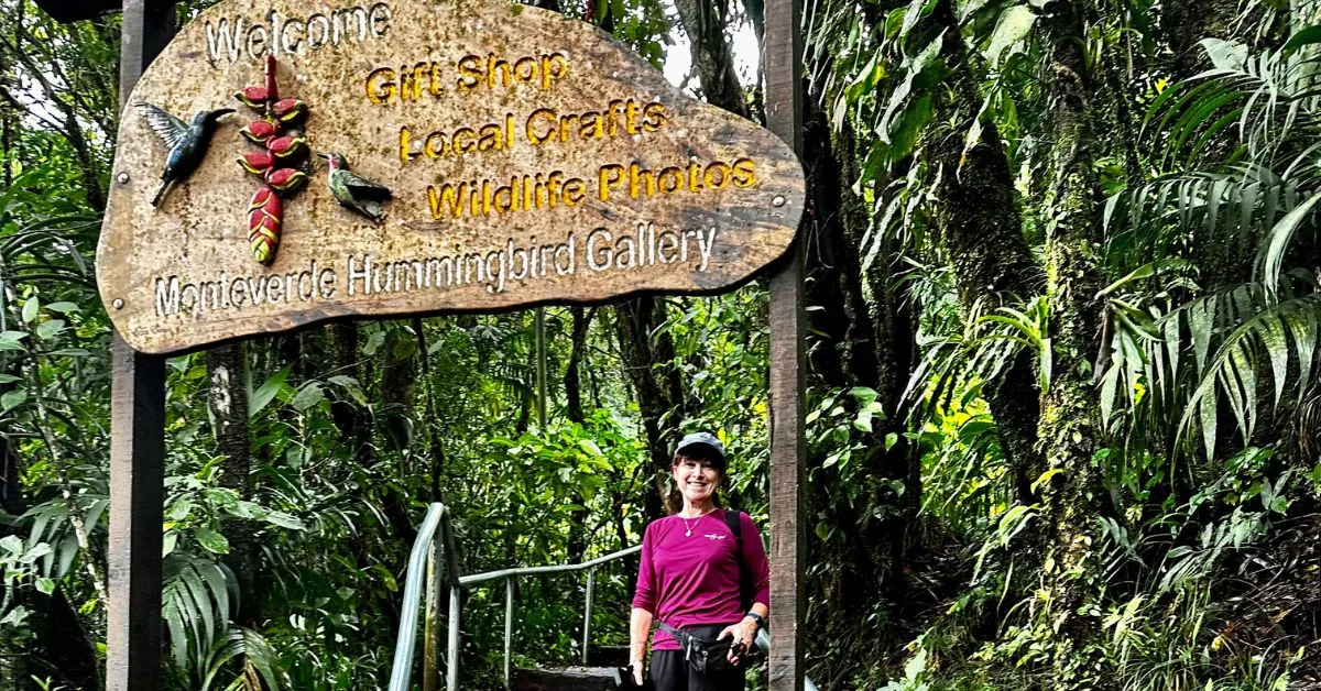 Woman is standing beneath a welcome sign to the Monteverde Hummingbird Gallery.