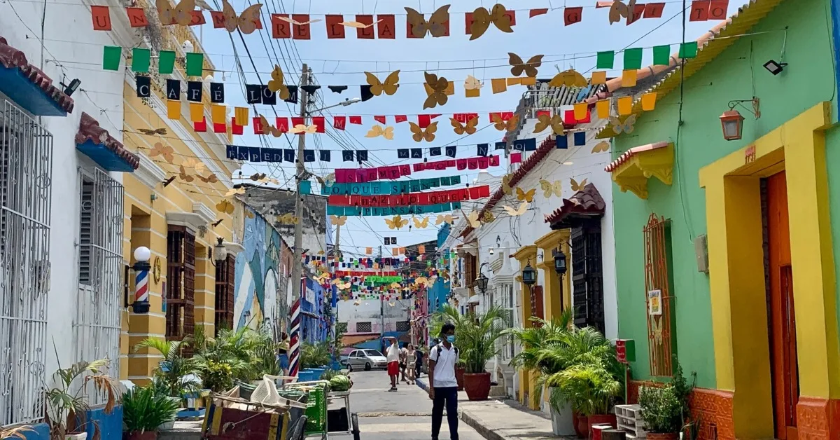 A street in Getsemani, with multi colored banners strung between buildings. The buildings are painted green, white and blue.