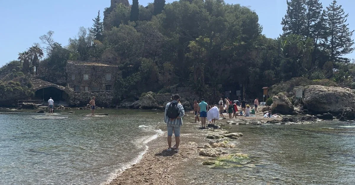 People walking on a stony water pathway to a tiny island