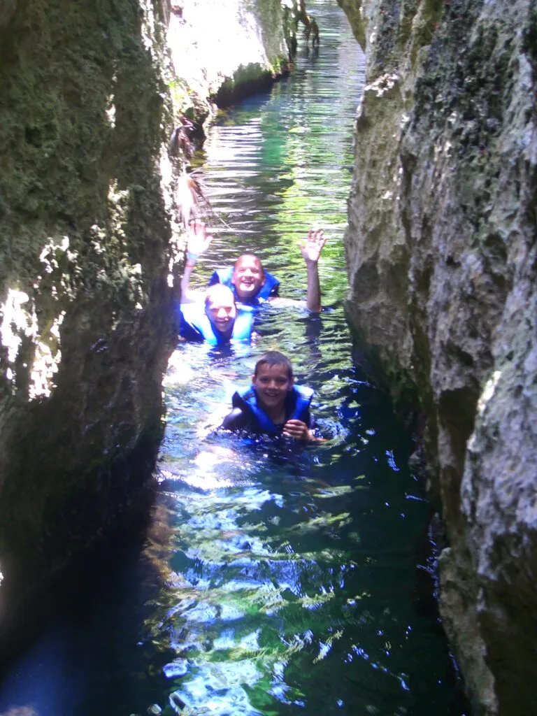 Family enjoying snorkeling in a water park and passing through high sided narrow rock area.