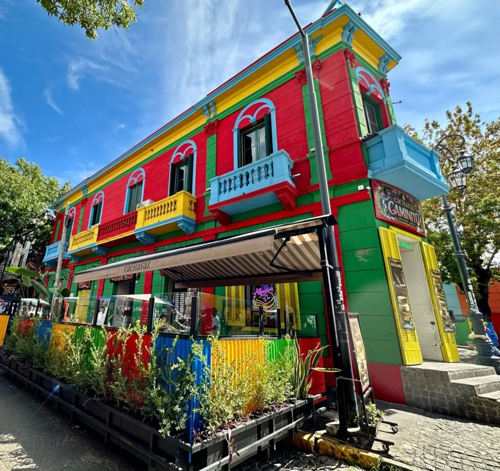 A traditional street corner pained in red, yellow and blue showcases the history of La Boca area of Buenos Aires. The building has pained balconies too in yellow and blue.