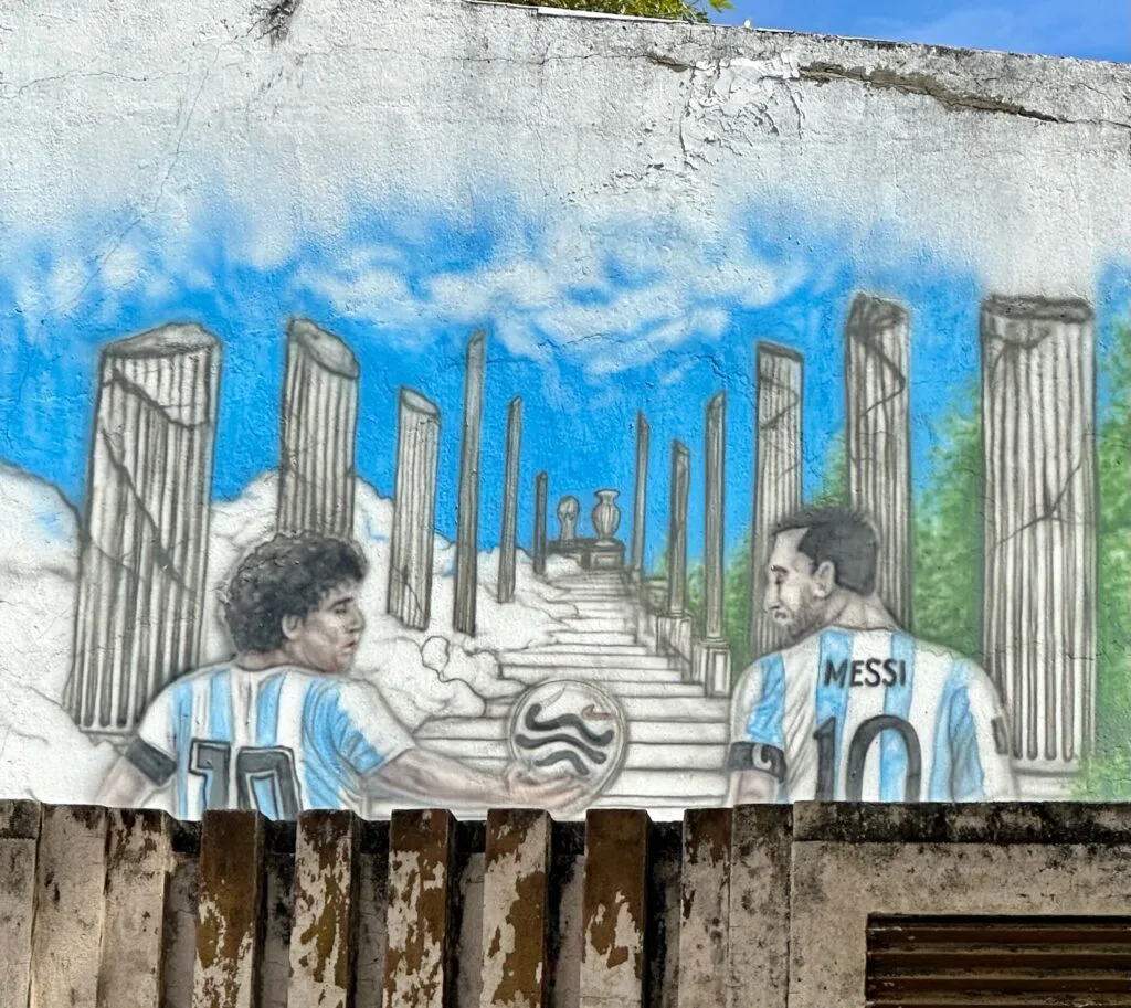 A mural painted on a street wall in Buenos Aires shows two football heroes Messi and Maradona. The men are walking up a staircase to the World Cup.