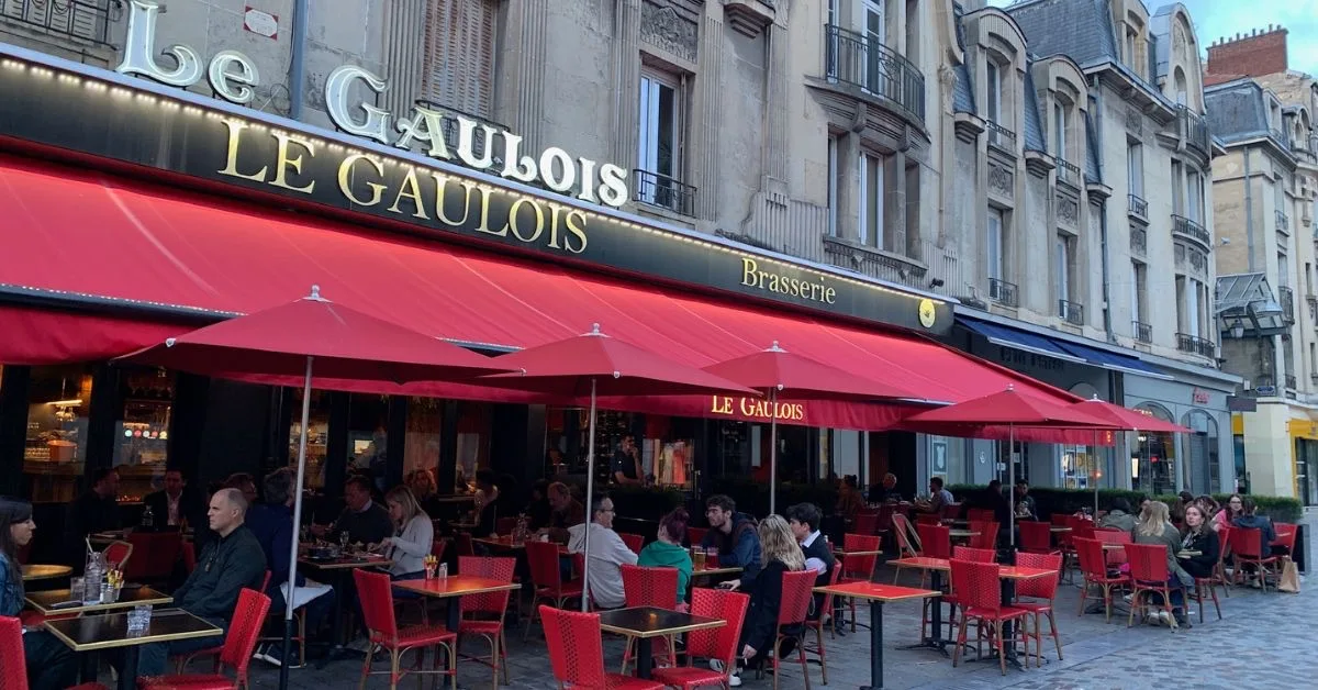 Outdoor Dining in Reims with tables and chairs under red awning and umbrellas for shade.
