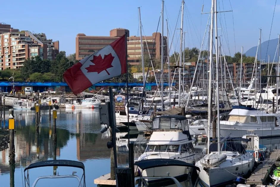 View of waterfront downtown in Vancouver with moored sail boats and behind high rise glass skyscrapers.
