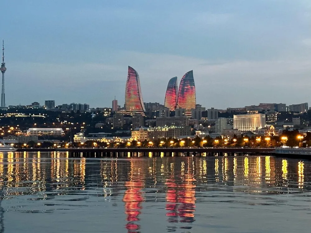Baku Azerbaijan city skyline with three flame towers showcasing new architecture in the capital city. Lights reflect red and yellow on the Caspian Sea.