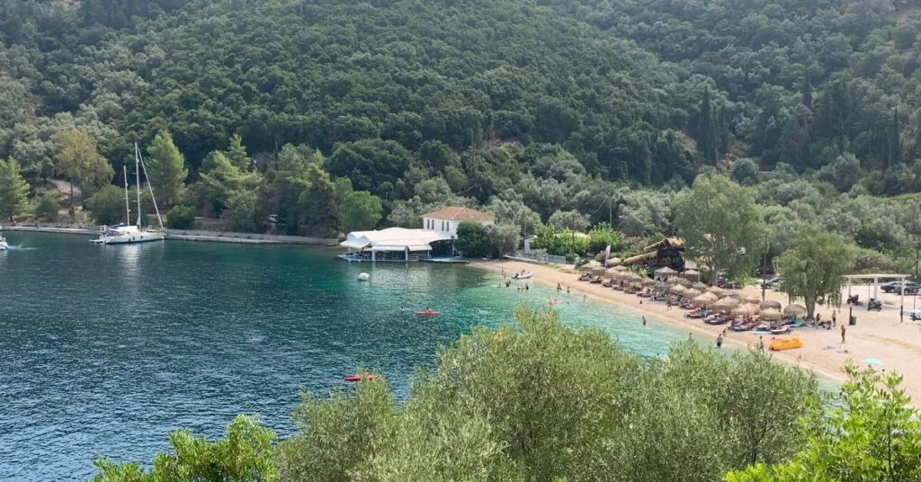 Looking down on small quiet beach from a viewpoint showing turquoise waters and straw umbrellas and a few people on the beach