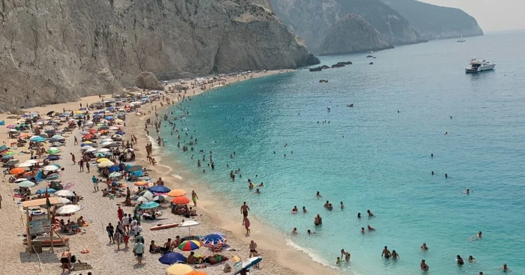 Crowded beach with lots of people under parasols or in the sea. cliffs at the side of the beach