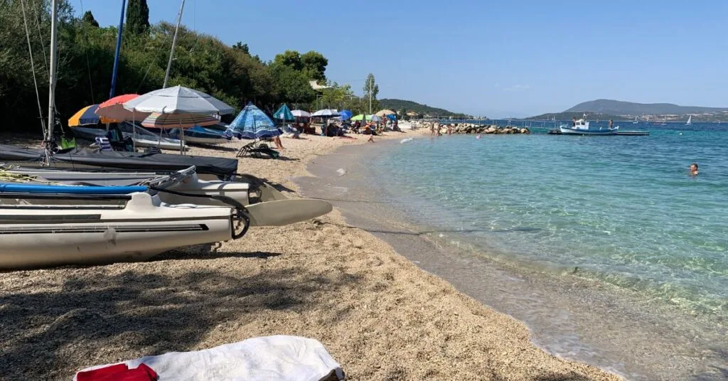 Small bay with sandy beach, small boats and turquoise sea. A few people on the beach under parasols or swimming