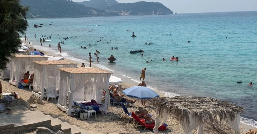 Day beds with canopies and narrow beach strip with people in the sea or relaxing on the beds or sand