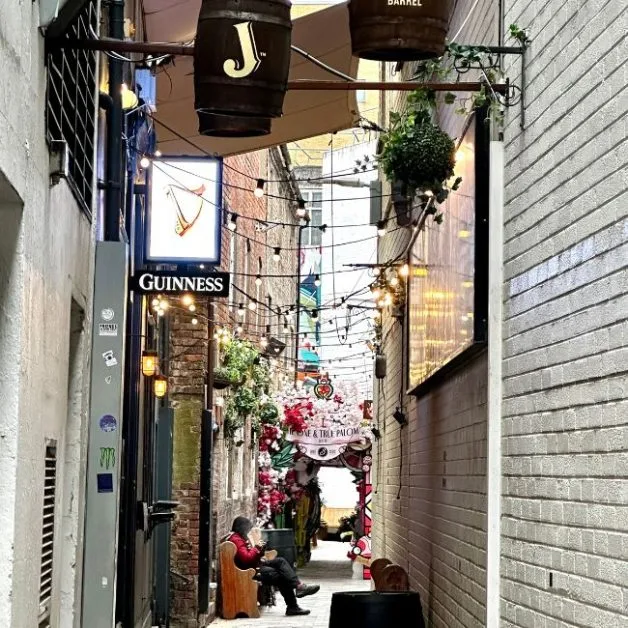 A brick lined side street in Belfast showing Guinness sign outside a pub and flowers around doorways.