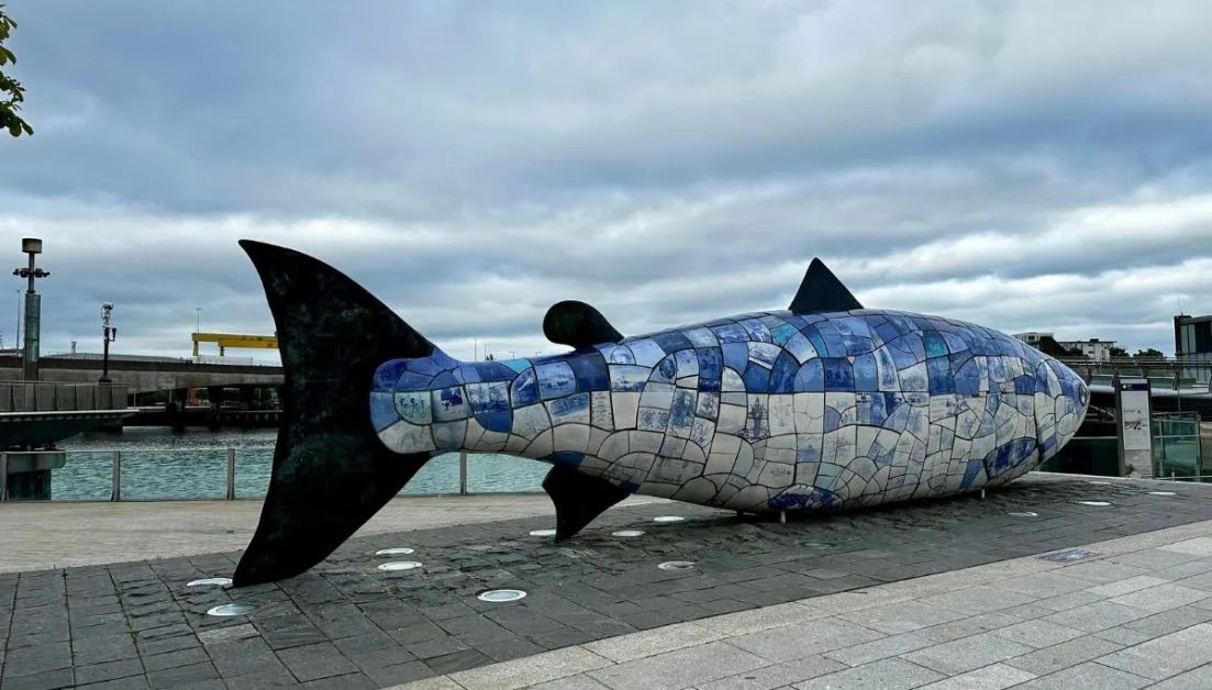 Street Art in Belfast the capital of Northern Ireland. A large metal fish in blue, silver and black sits on the quayside.