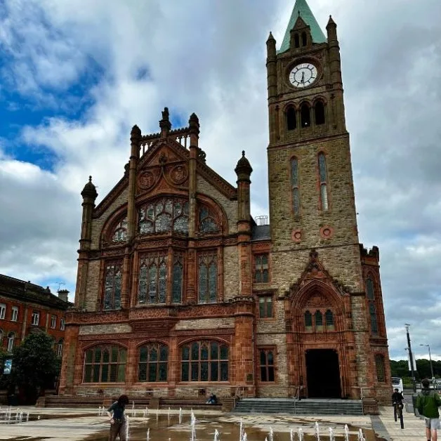 A red and brown stone building with clocktower and stain glass windows in Derry, Northern Ireland.