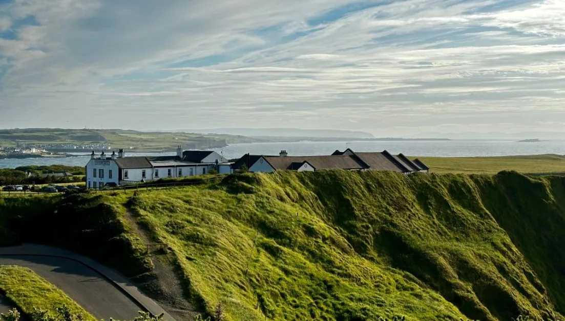 Whitewashed hotel at Giants Causeway in Northern Ireland. Green rugged cliffs lead down from the hotel to the ocean.