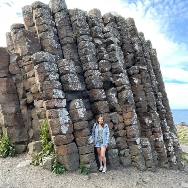 Jude standing at the base of a 10 meter high basalt rock tower at Giants Causeway.