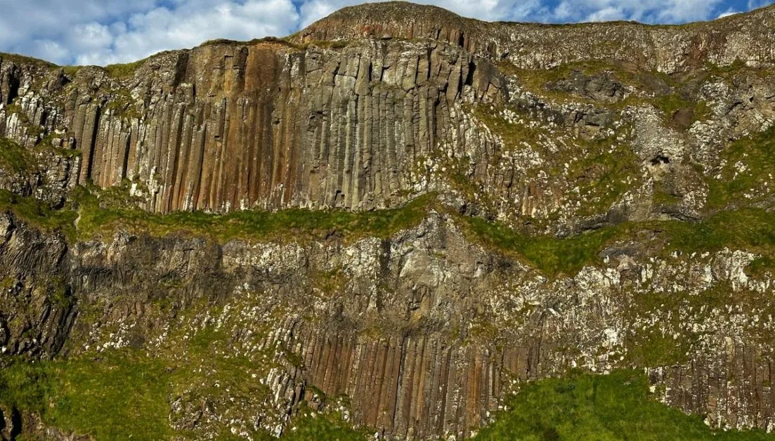 Sheer brown, grey basalt rock cliffs with pockets of grass.