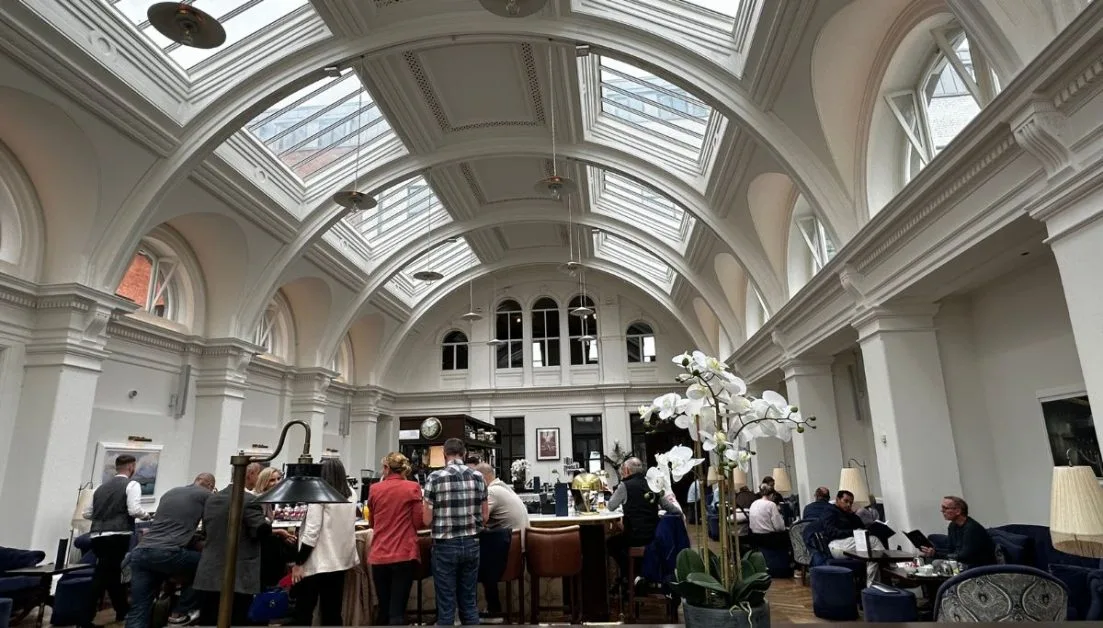 Arched roof with glass panels and people enjoying a drink at the bar in the Titanic Hotel drawing room.
