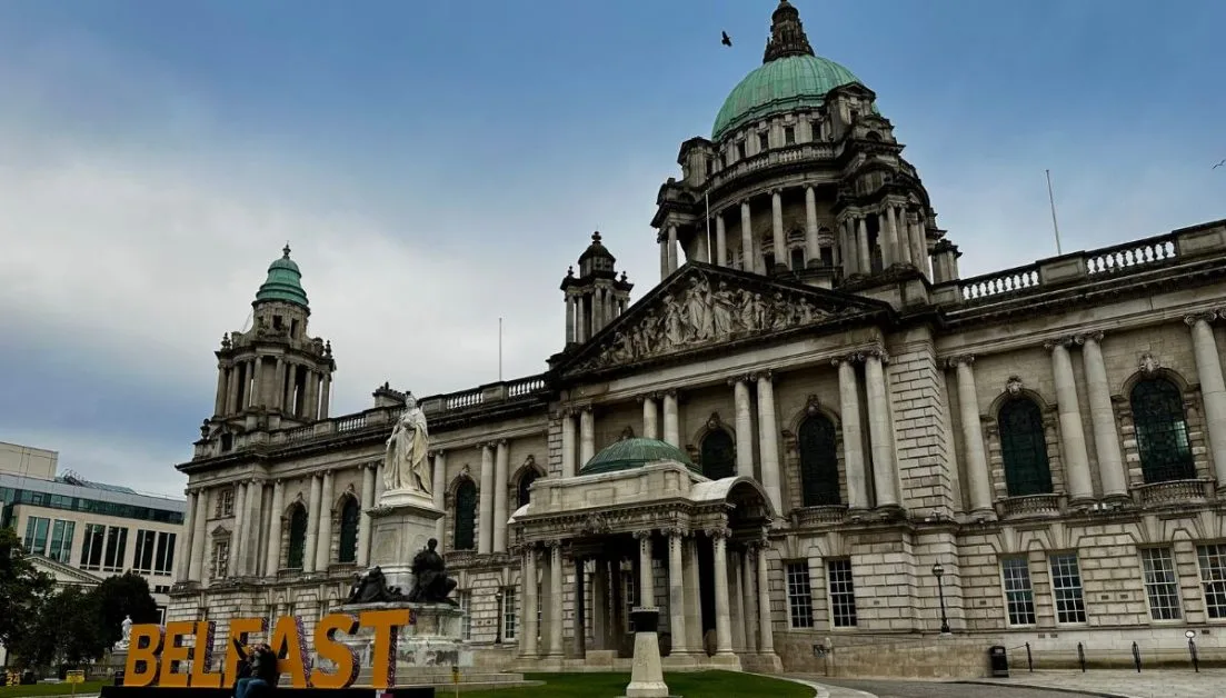 A large orange sign 'Belfast' in front of the city hall, with large scale column facade.