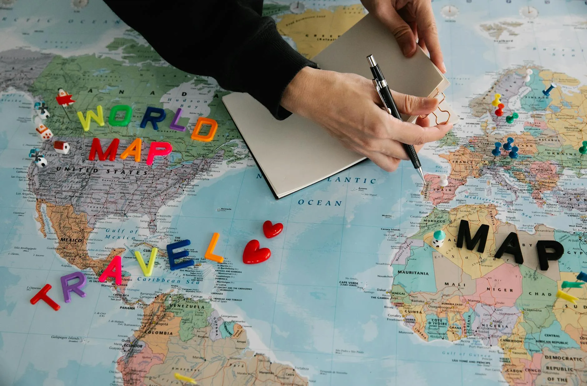 Hands with pen and notebook planning travel over a world map