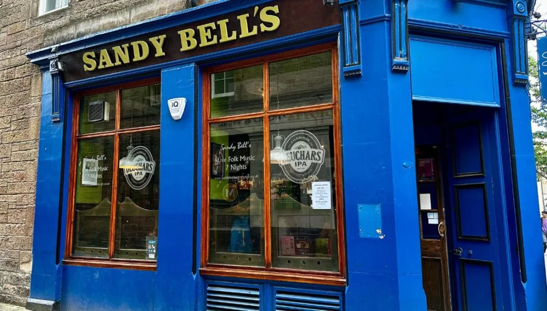Sandy Bells pub in Edinburgh offers folk music performances every night. The building is painted a bright blue and the name of pub is painted in gold.