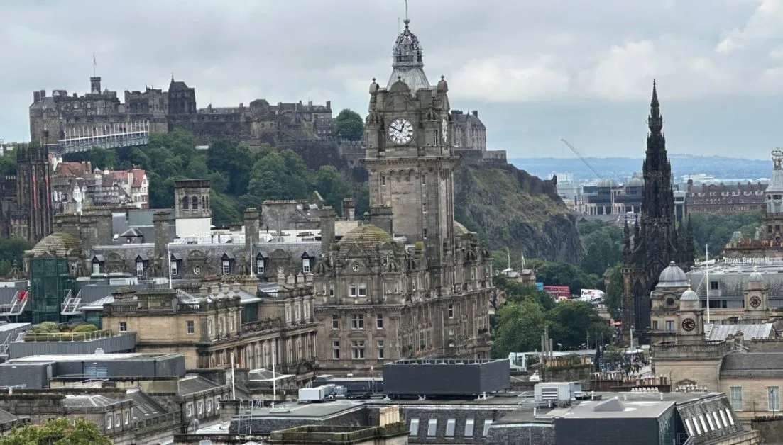 View of city of Edinburgh with Balmoral Hotel and its clock in the forefront and Edinburgh castle high on a hill behind.