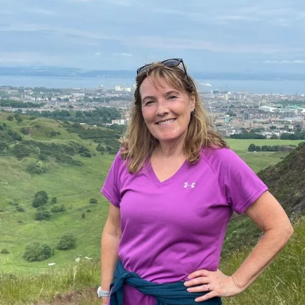 A woman at the top of Arthur's Seat with sweeping view of Holyrood Park and the city behind. One of the most popular cheap things to do in Edinburgh - in fact its free.