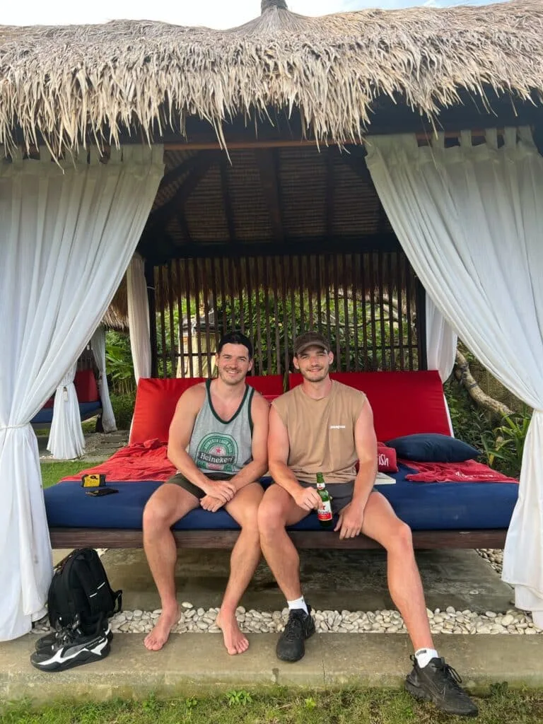 Two men sitting under a thatched roof in Bali having a beer