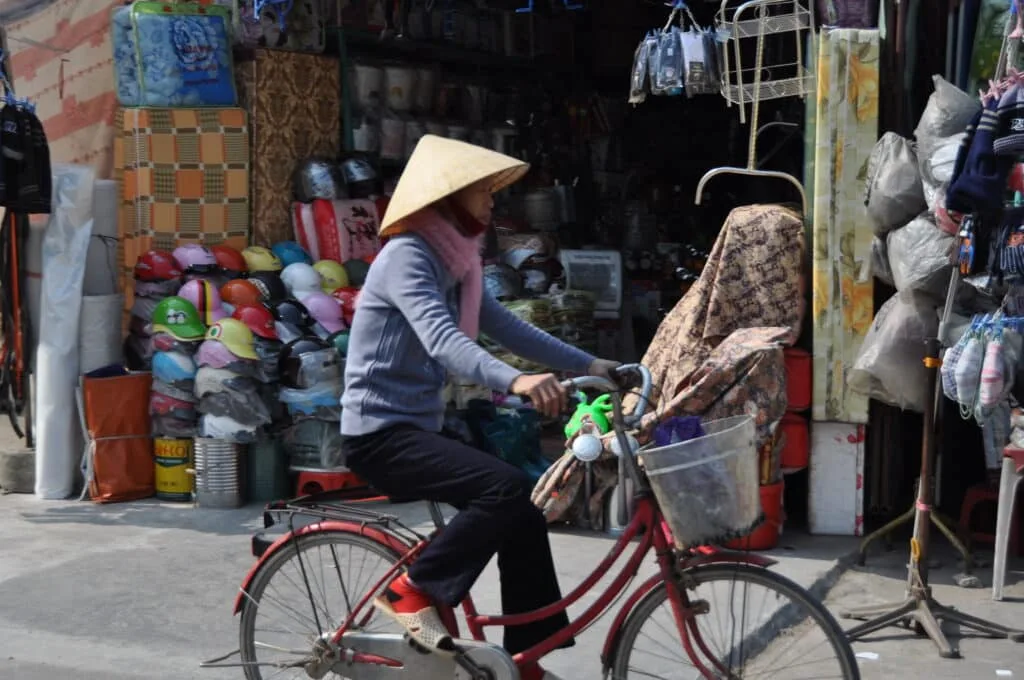 A Vietnamese woman is cycling through Hanoi wearing a cone hat which shades her face from the sun.