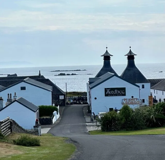 Whitewashed buildings next to the sea are where Ardberg whisky is distilled. Malt towers are visible.