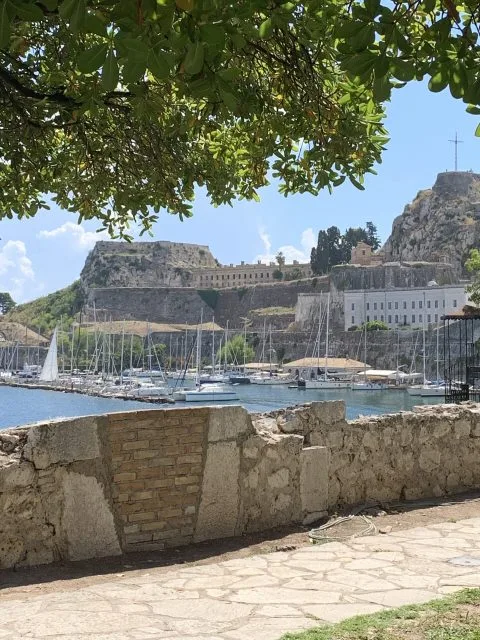 View from a promenade under the shade of trees over to an old fortress.