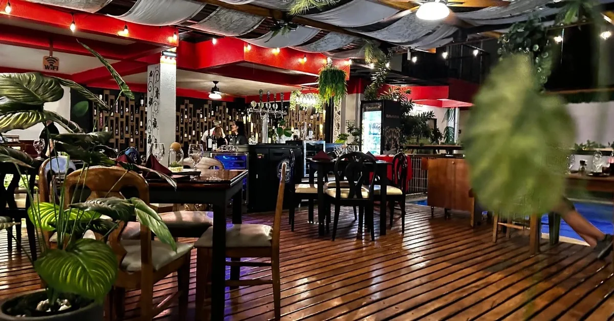 Interior of Maria Bonita Steakhouse with wooden floors and tables set for dinner. Canopy roof with red painted supports add character.