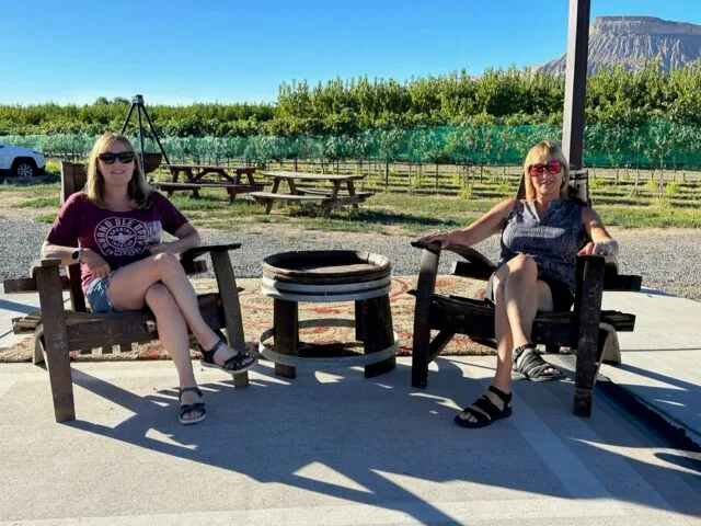 Palisade stop over on roadtrip from Denver for wine tasting. Two woman sitting in vineyard.