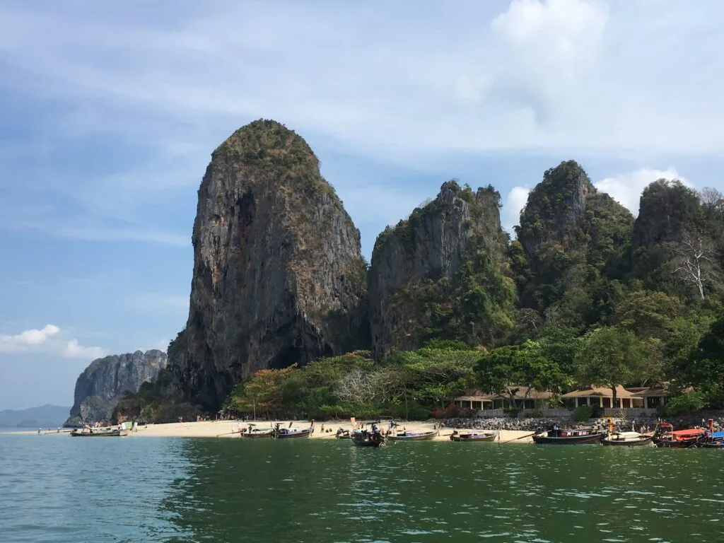 A cave and beach structure with 4 large stone peaks jutting out of the ground behind a beach with a sandy cove.