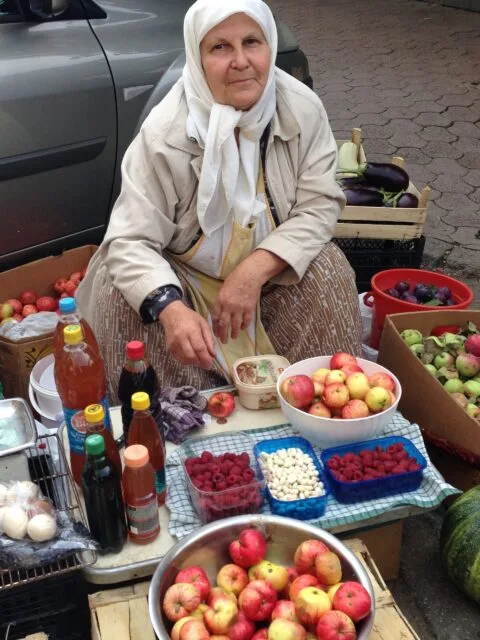 A woman selling fruit and vegetables and bottles of home-made drinks on a street in Sarajevo.