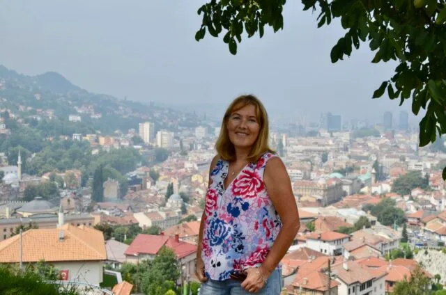 Woman standing on a Yellow Fortress hill top in Sarajevo with the city behind her and its roof tops in red tile.