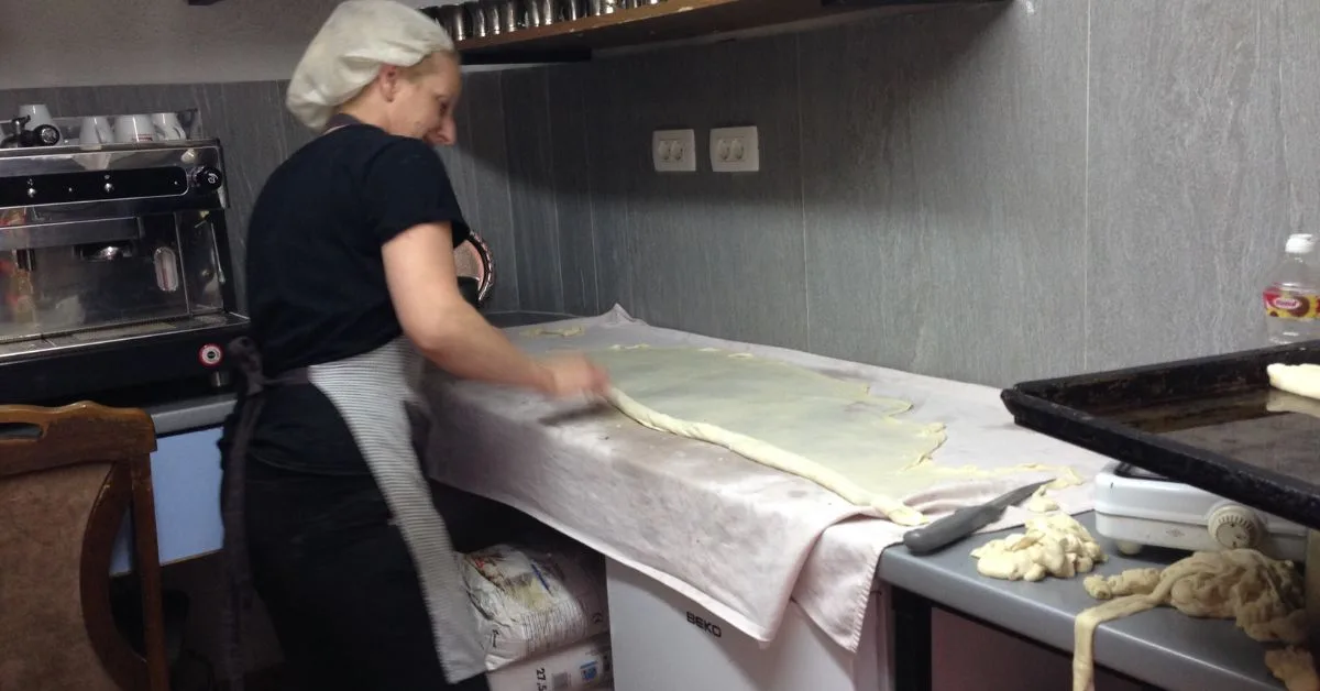 A Woman stretching raw dough to make Borek in kitchen in Sarajevo.