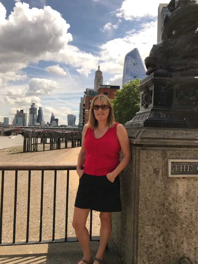 Woman paused against a metal fence area while walking in London next to the Thames River.