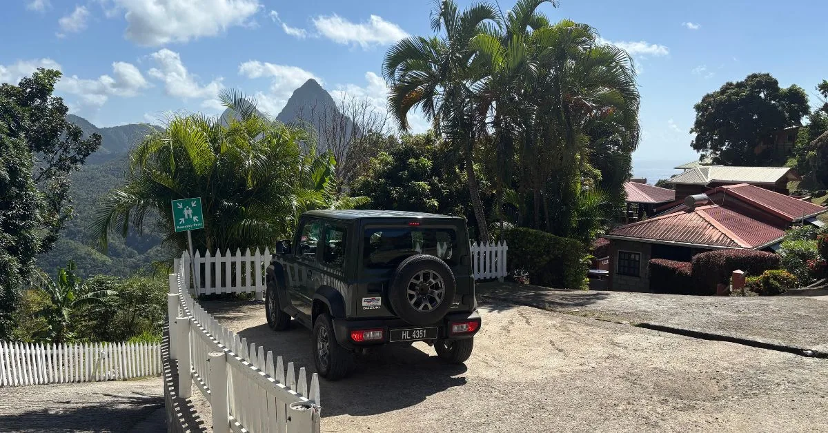 Jeep parked up next to a white fence with the Pitons of St Lucia in the background.