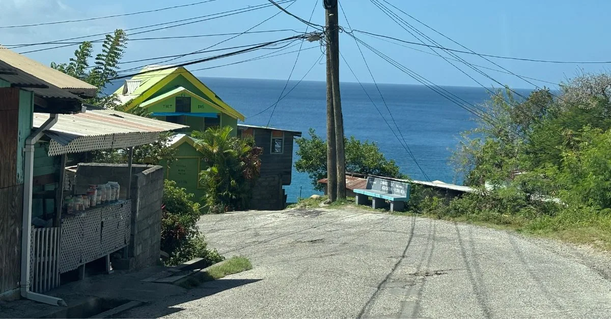 Road in St Lucia showing a sharp turn to the left. Sea in the background and house by the side of the road.