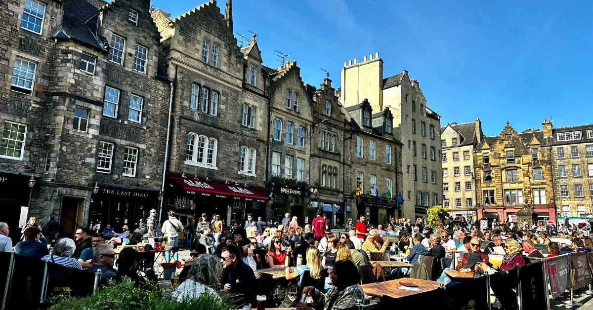 People sitting at cafe seating outside in The Grassmarket area of Edinburgh.