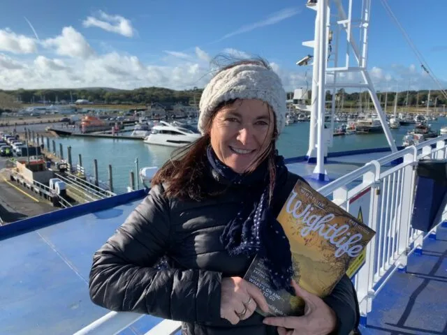 A woman is on a ferry heading to the Isle of Wight. She is holding a travel brochure.